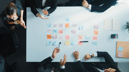 Top view of investor writing white board to present project and putting hand together with professional business team to celebrate successful project at meeting table with sticky note.の写真素材