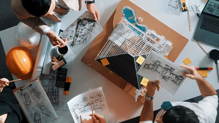 Top view of manager handing blueprint to professional engineer team at meeting table with house model and project plan. Group of architects discussing design while receiving document.の写真素材