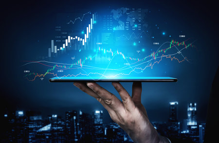 A hand holds a tablet displaying dynamic digital charts and graphs against a city backdrop, representing the future of business and financial analysis in a tech-driven world.の写真素材