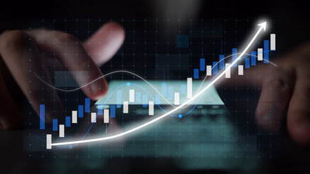 Close-up view of hands interacting with a smartphone displaying stock market trends and financial graphs, showcasing the significance of technology in investment strategies.の写真素材