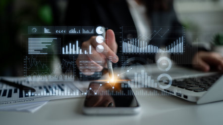 A dedicated business professional reviews key data trends using advanced analytics on a smartphone and laptop in a contemporary office environment.の写真素材
