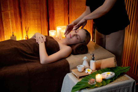 Caucasian woman enjoying relaxing anti-stress head massage and pampering facial beauty skin recreation leisure in warm candle lighting ambient salon spa in luxury resort or hotel. Quiescentの写真素材