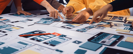 A diverse group of individuals collaborates on user interface mockups at a table filled with notes...