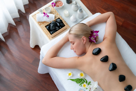 Panorama top view hot stone massage at spa salon in luxury resort with day light serenity ambient, blissful woman customer enjoying spa basalt stone massage glide over body. Quiescentの写真素材