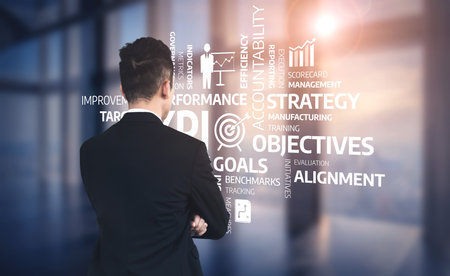 A businessman stands thoughtfully in a modern office, analyzing strategic goals and objectives showcased through graphics and charts, emphasizing planning and performance. Tesselの写真素材