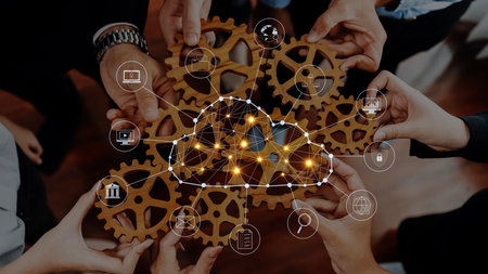 A group of diverse professionals join hands around interconnected gears, symbolizing teamwork and...