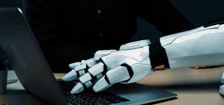 A close-up of a robotic hand interacting with a laptop, showcasing the blend of advanced technology and human-like capabilities in a modern office environment.の写真素材
