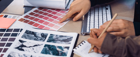 A creative workspace scene showcasing designers collaborating on color palettes, analyzing swatches, and jotting notes for their next artistic project, fostering teamwork.の写真素材