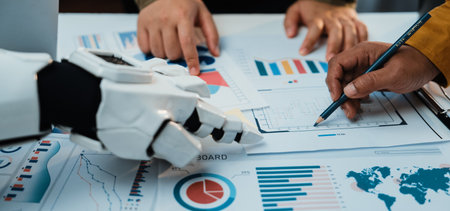 A futuristic collaboration scene features human and robotic hands analyzing various data visualizations during a business meeting, showcasing innovation and teamwork.の写真素材