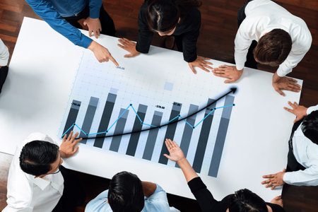 A diverse group of professionals collaborates over a business growth chart during a strategy meeting, highlighting teamwork and data analysis in an office setting.の写真素材