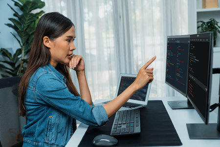 Young Asian girl of IT developer pointing online information on pc with coding program data application on website project, wearing jeans shirt. surrounded by safety programing two screens.の写真素材