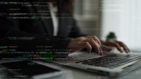 A focused programmer types on a laptop, immersed in software development, highlighted by lines of code illuminating their creative workspace in a modern office setting.の写真素材