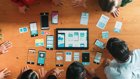 Top view of software developer team looking Ux Ui design for mobile phone interface from tablet while comparing and planning wireframe prototype designing together at creative workplace. Convocation.の写真素材