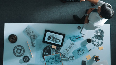 Top down view of smart engineer talking about turbine engine design while standing at meeting table with gear. Aerial view of technician discussing about electronic generator structure.の写真素材