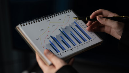A person holds a notepad showcasing growth trends represented through various graphs and charts,...