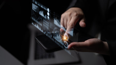 A businessman interacts with financial data on a smartphone, illuminated by virtual graphs and...