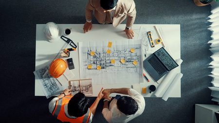 Top down aerial view of smart architect engineer team pointing and discussing about building construction. Group of diverse people working together to plan and design by using blueprint.の写真素材