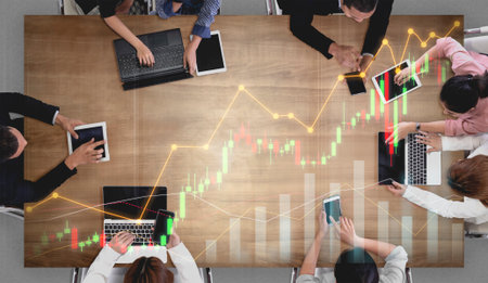 A diverse business team engages in a strategic meeting, utilizing smartphones and laptops to analyze financial data and market trends, fostering collaboration and idea-sharing.の写真素材