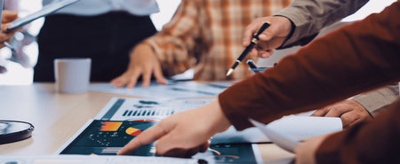 A group of diverse business professionals engaging in a collaborative meeting, analyzing charts and documents on a table in a vibrant office atmosphere.の写真素材
