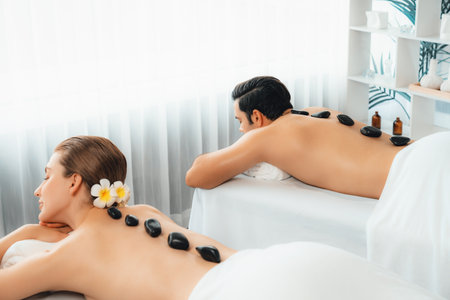 Hot stone massage at spa salon in luxury resort with day light serenity ambient, blissful couple customer enjoying spa basalt stone massage glide over body with soothing warmth. Quiescentの写真素材