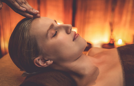 Closeup caucasian woman enjoying relaxing anti-stress head massage and pampering facial beauty skin recreation leisure in warm candle lighting ambient salon spa in luxury resort or hotel. Quiescentの写真素材