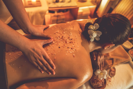 Woman customer having exfoliation treatment in luxury spa salon with warmth candle light ambient. Salt scrub beauty treatment in Health spa body scrub. Quiescentの写真素材