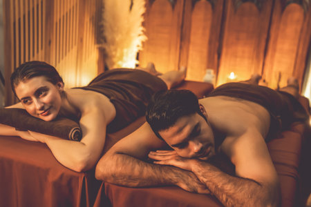 Caucasian couple customer enjoying relaxing anti-stress spa massage and pampering with beauty skin recreation leisure in warm candle lighting ambient salon spa at luxury resort or hotel. Quiescentの写真素材