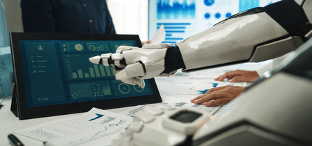 A robot collaborates with a human team in a modern office setting, analyzing data on a touchscreen display, showcasing technology's role in business productivity.の写真素材