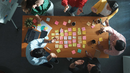 Top view of diverse business team putting hand together and clapping hand while brainstorming marketing idea or creative startup project by using sticky notes and stick at meeting table. Convocation.の写真素材