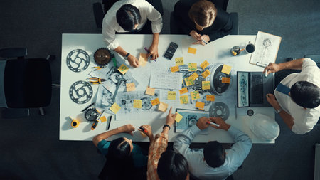 Top view of smart engineer team in casual cloth talking about turbine engine structure at table with metal gear, calculator, sticky notes. Group of technician taking a note in meeting.の写真素材