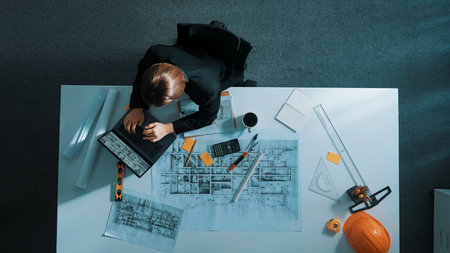 Top view of businesswoman hand blueprint to engineer sitting at meeting table with project plan, equipment and safety helmet. Aerial view of manager explain about building construction.の写真素材