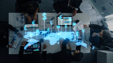 A diverse business team engages in collaboration over financial data, reviewing charts and currency symbols in a modern office, emphasizing teamwork and strategy.の写真素材