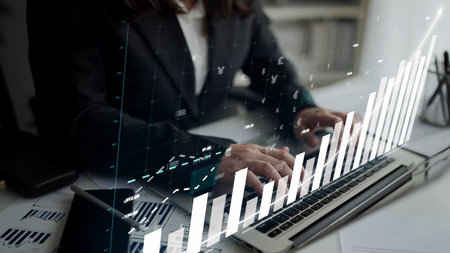 A business professional examines financial data and growth graphs on a laptop in a contemporary...