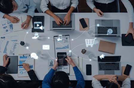 A vibrant business meeting scene featuring diverse individuals engaging with laptops and devices, surrounded by charts and visual communication elements for effective strategy planning.の写真素材