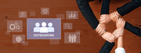 Hands join together to symbolize collaboration and teamwork in a business environment, representing the concept of outsourcing and partnership on a wooden table backdrop.の写真素材