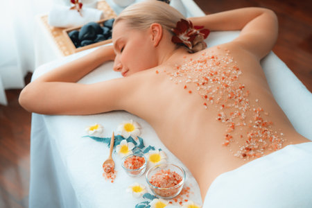 Woman customer having exfoliation treatment in luxury spa salon with warmth candle light ambient. Salt scrub beauty treatment in health spa body scrub. Quiescentの写真素材