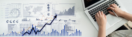 A professional workspace featuring a laptop with hands typing, surrounded by data visualizations,...