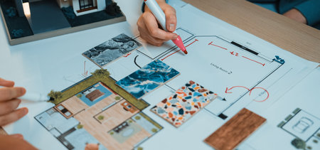 Engaging scene of hands collaborating on an architectural floor plan. Colorful swatches and detailed layout sketches showcase creative design processes in a modern workspace.の写真素材