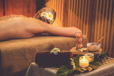 Woman customer having exfoliation treatment in luxury spa salon with warmth candle light ambient. Salt scrub beauty treatment in Health spa body scrub. Quiescentの写真素材