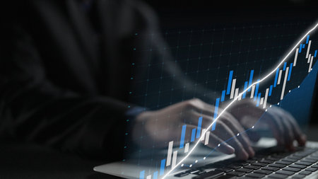 A close-up view of hands typing on a laptop with an overlay of a stock market graph displaying a positive growth trend, symbolizing business analysis and investment decisions.の写真素材