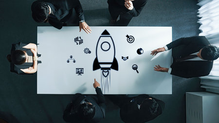 A dynamic business team gathers around a modern table, discussing innovative strategies with a rocket graphic symbolizing growth and potential in a collaborative environment.の写真素材