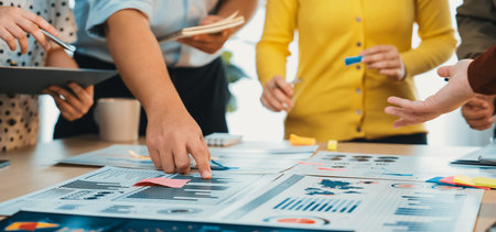 A dynamic group of professionals collaborates in a bright office space. They analyze various graphs and charts while discussing strategies using sticky notes and documents.の写真素材