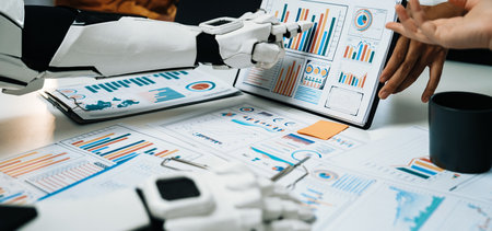 A robotic arm engages in a business meeting, analyzing various data graphs and charts alongside human hands, showcasing the future of technology in collaboration.の写真素材