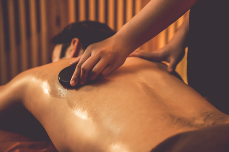Hot stone massage at spa salon in luxury resort with warm candle light, blissful man customer enjoying spa basalt stone massage glide over body with soothing warmth. Quiescentの写真素材