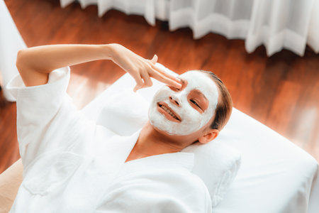 Serene daylight ambiance of spa salon, top view woman lying on massage table smiling and rejuvenating with face cream spa massage. Facial skin spa treatment and beauty care concept. Quiescentの写真素材