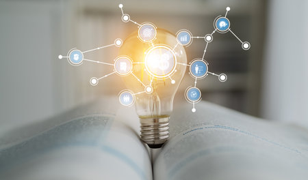 A creative representation of innovation, this image features a glowing light bulb atop an open book, symbolizing the connection between knowledge and digital advancements in society. Tesselの写真素材