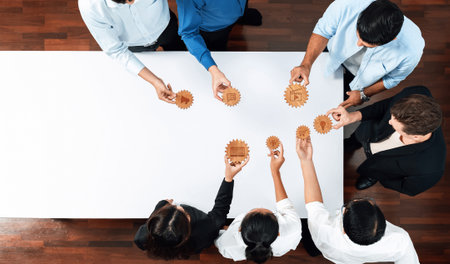 Aerial view of a diverse team of business professionals engaging in a collaborative strategy session with gears on a table, symbolizing teamwork and innovation in the workplace.の写真素材