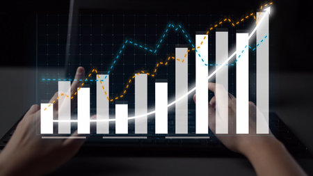 Hands on a laptop keyboard amidst visual representations of financial growth, illustrating business...