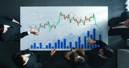 Business professionals collaborate over financial graphs and charts in a bright office environment,...