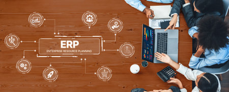A diverse business team collaborates on an enterprise resource planning project, utilizing laptops and various technology icons on a wooden table.の写真素材
